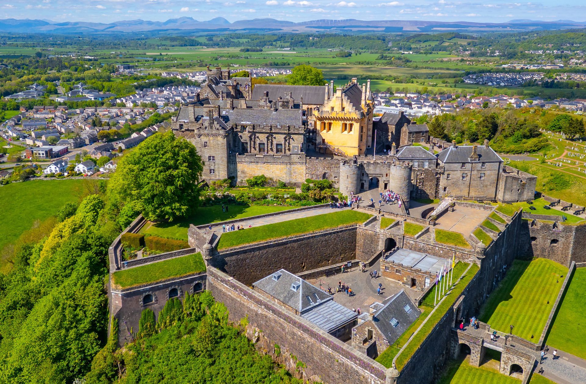 Aerial view of a large stone castle with green lawns overlooking a countryside landscape