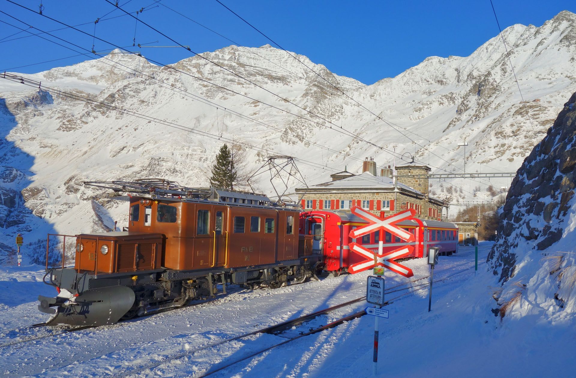 Snowy mountain railway with an orange locomotive and red caboose in bright sunlight