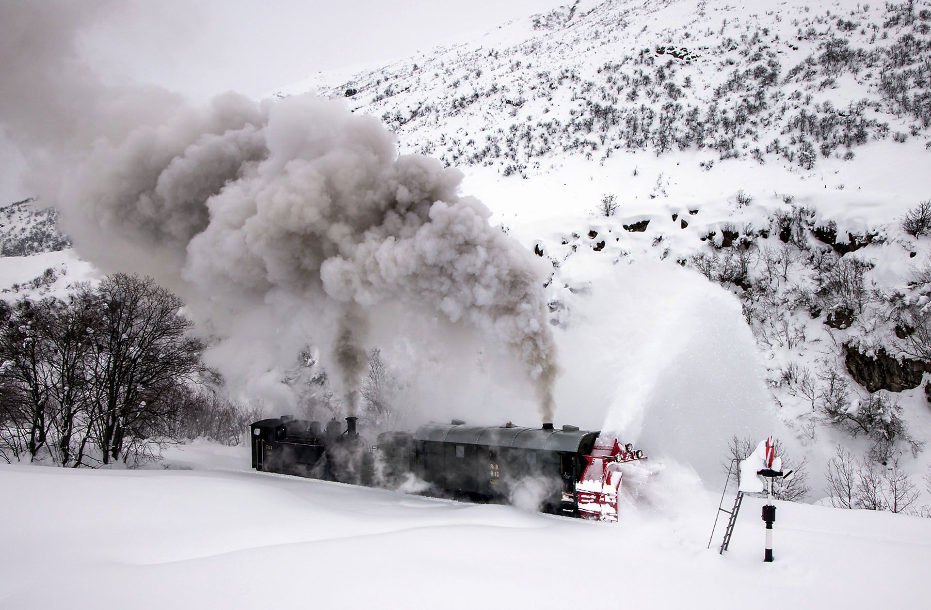 Snow-covered train emitting thick smoke in a mountain landscape