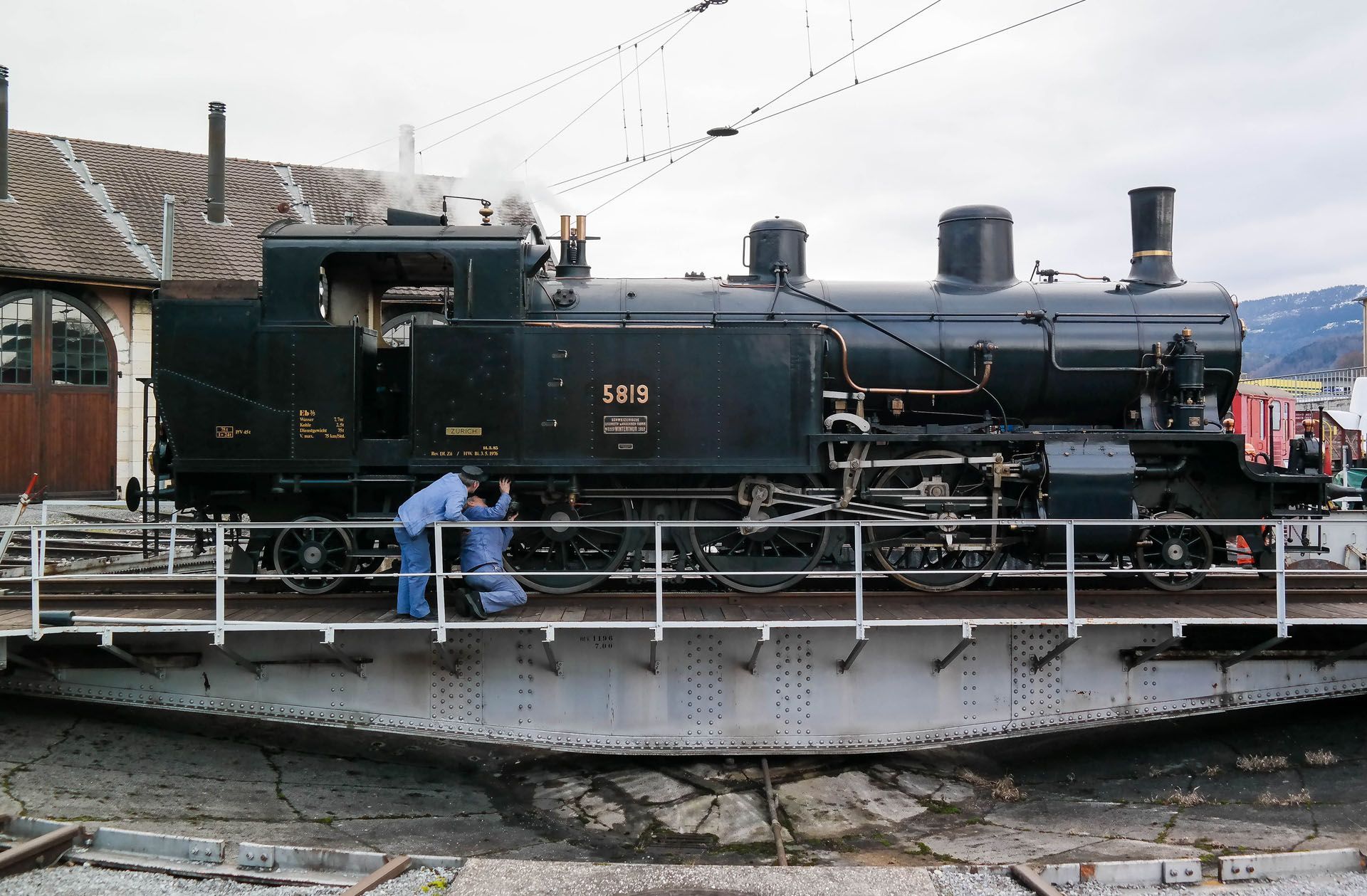 Black steam locomotive on a turntable with a worker in blue overalls beside it