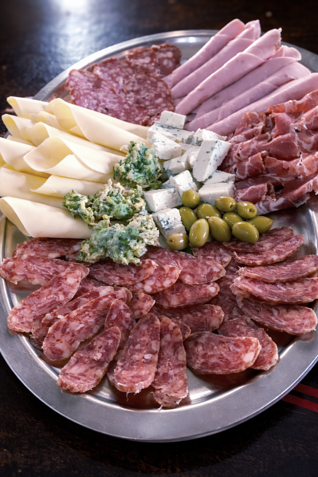 Una bandeja con una selección de embutidos variados, jamón cocido en lonchas, lonchas de queso enrolladas, queso azul 