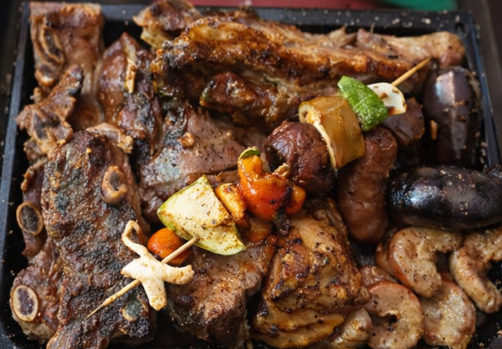 Una bandeja de carnes variadas a la parrilla, que incluye costillas, salchichas y brochetas de verduras