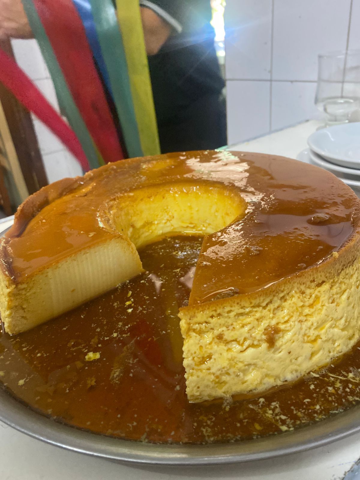Un flan circular con una rebanada retirada, cubierto con salsa de caramelo, servido en una fuente de metal.