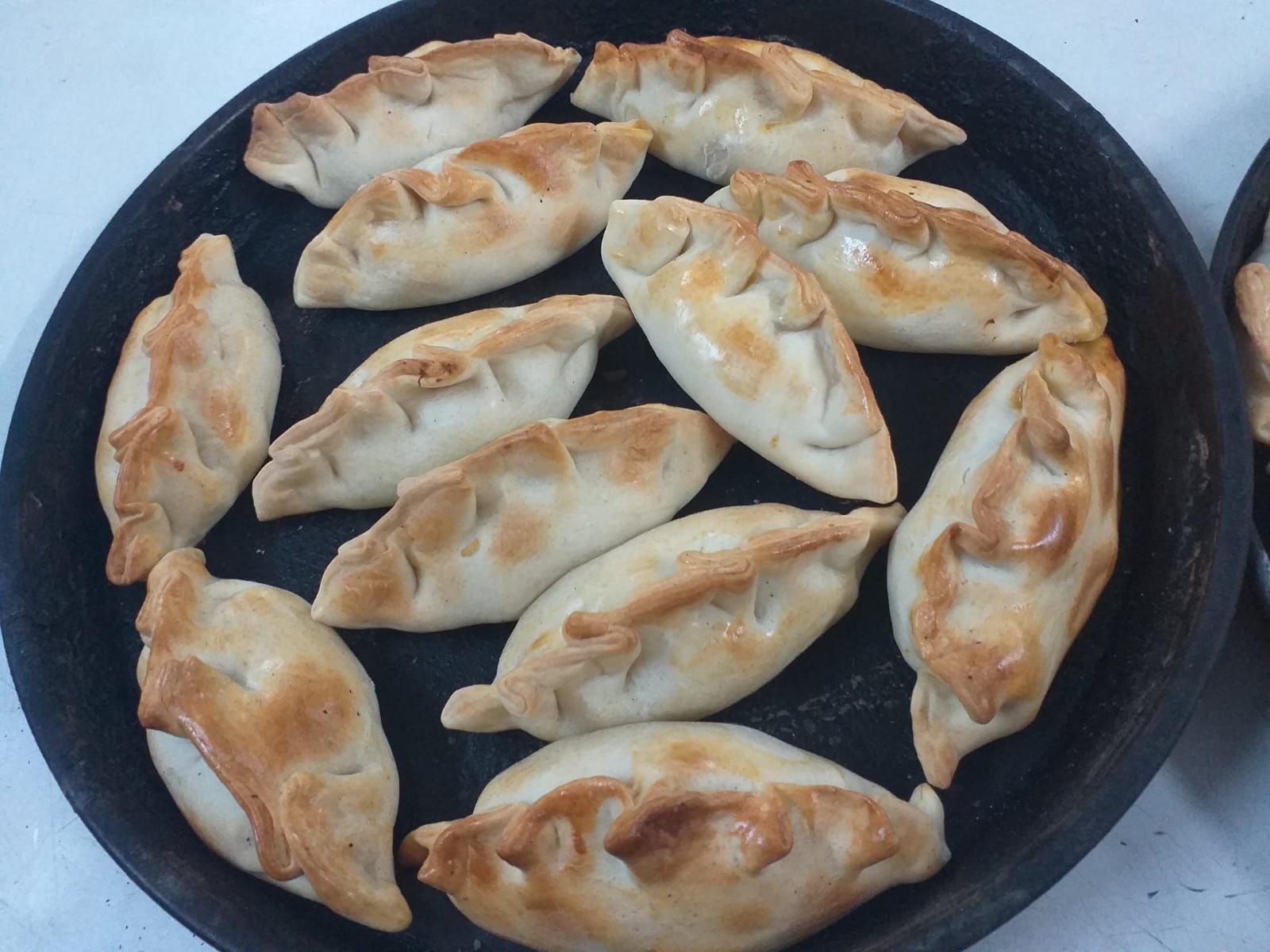 Una bandeja redonda llena de varias empanadas doradas y rizadas, dispuestas en círculo.