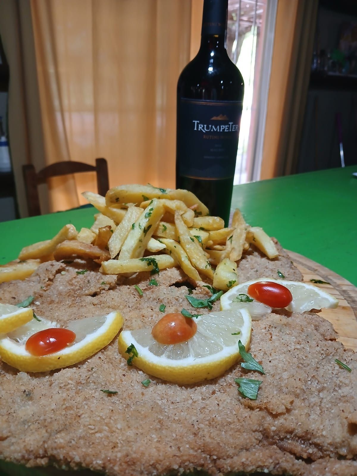 Escalope empanado con patatas fritas, adornado con rodajas de limón y tomates cherry, servido con una botella de vino tinto.