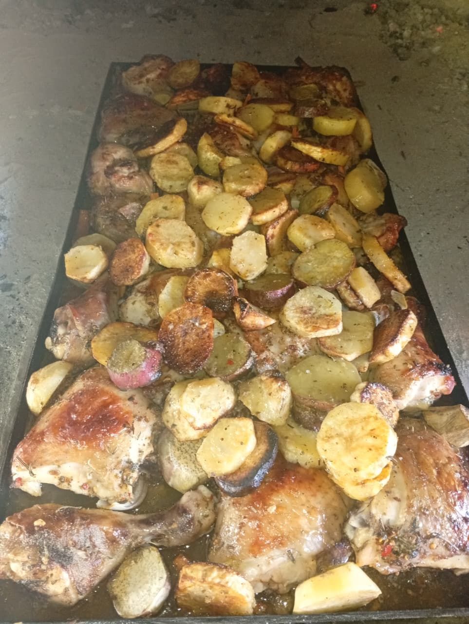 Una bandeja para hornear llena de trozos de pollo asado y patatas en rodajas, relucientes de aceite y condimentos.