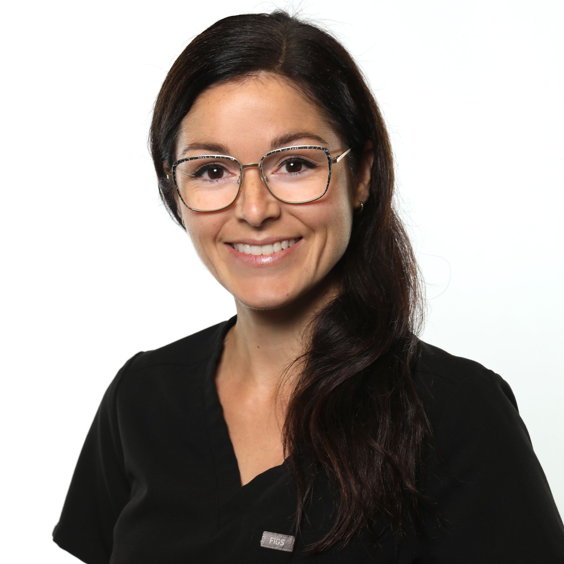 Une femme aux cheveux noirs et aux lunettes sourit, vêtue d'un haut de gommage noir, sur fond blanc.