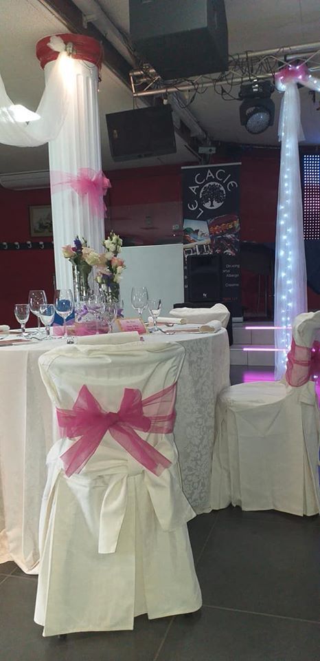 Sala banchetti decorata con sedie bianche, fiocchi rosa e colonne drappeggiate per un evento formale.