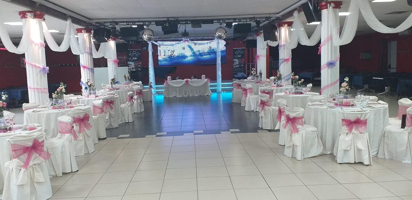 Sala per banchetti decorata con tavoli apparecchiati in rosa e bianco e un palco illuminato in fondo.
