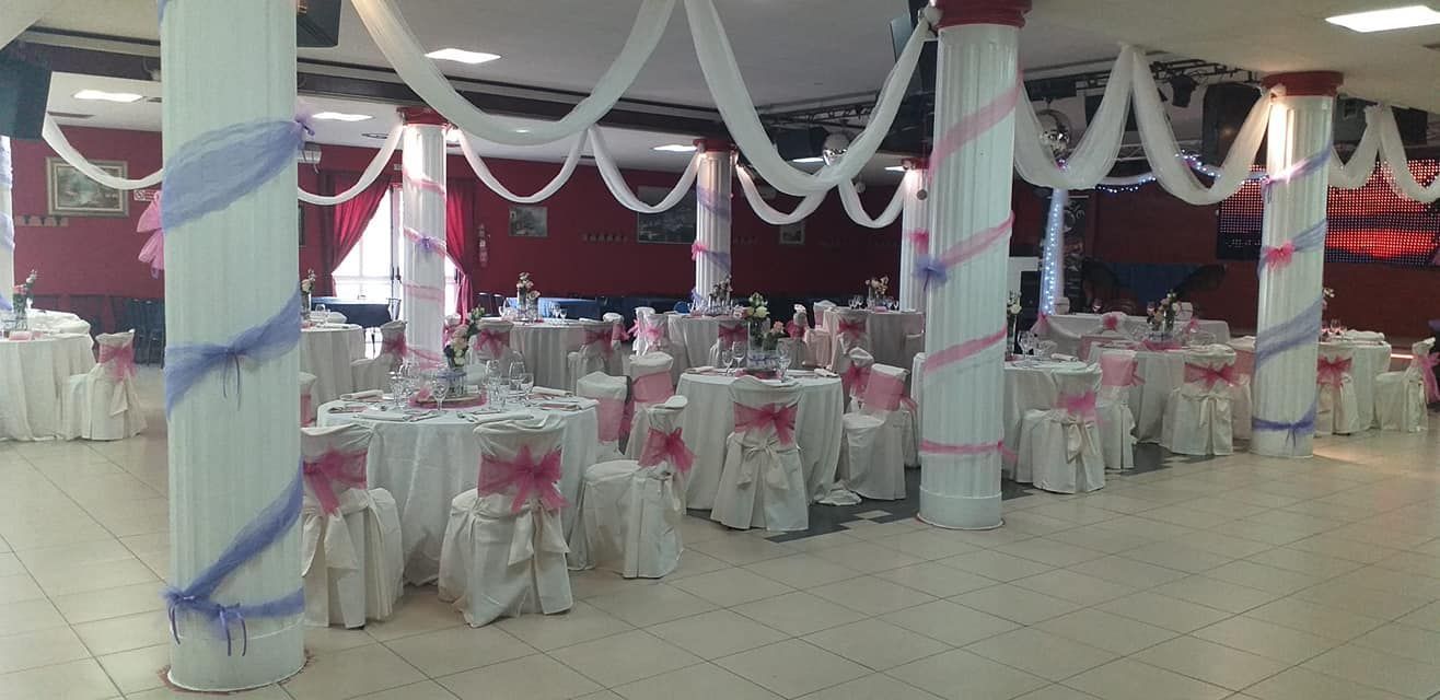 Sala per banchetti decorata con coprisedie rosa e bianchi e soffitto drappeggiato con tessuti.