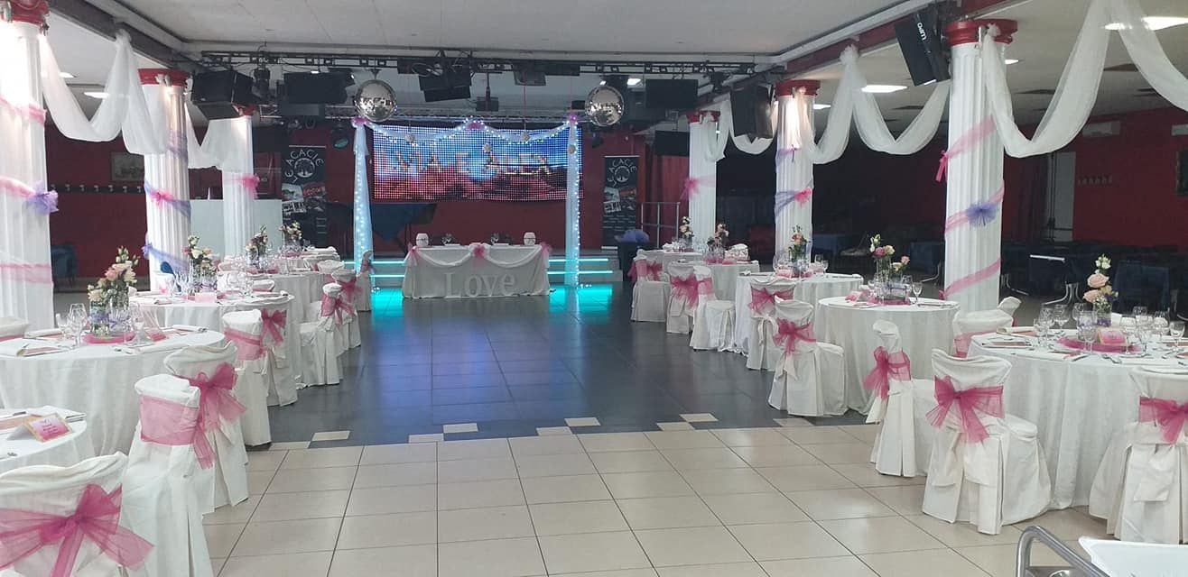Sala per banchetti decorata con tavoli rotondi, sedie bianche e una pista da ballo centrale illuminata con luci rosa e blu.