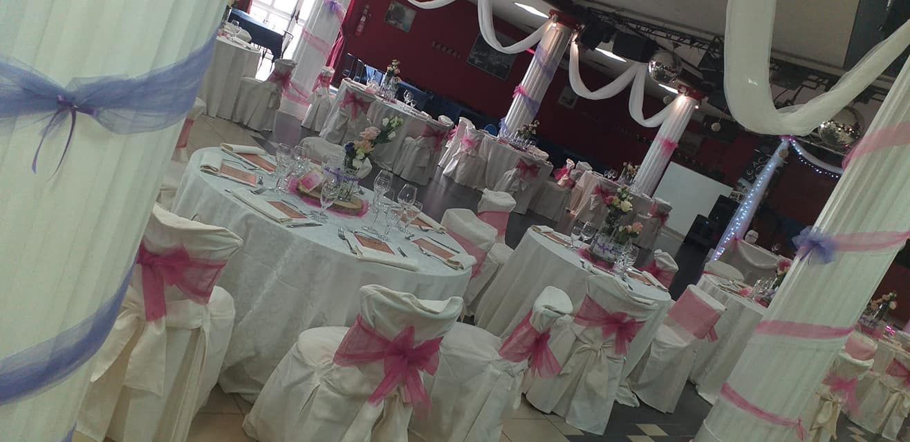 Sala da banchetto decorata con file di sedie ricoperte di bianco legate con fiocchi rosa e tavoli apparecchiati per un evento