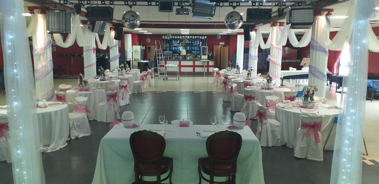 Sala per banchetti decorata con tavoli apparecchiati in bianco e rosa e una pista da ballo lucida.