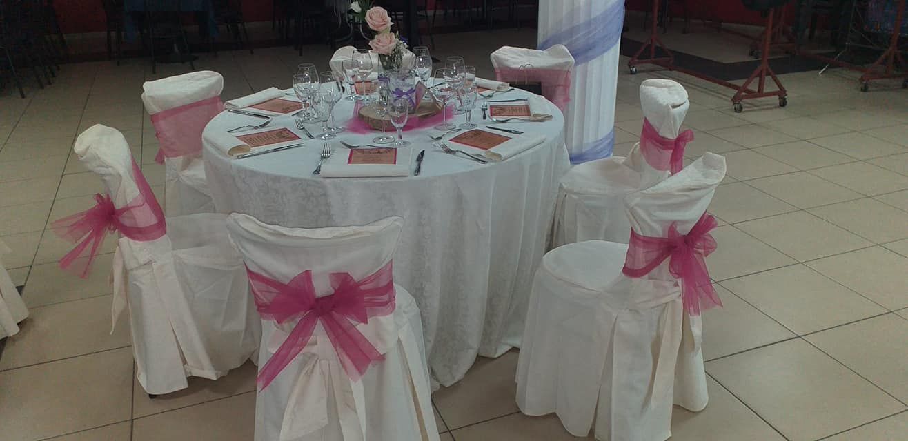 Tavolo rotondo con coprisedie bianchi e fiocchi rosa, apparecchiato per un'elegante esposizione di dolci