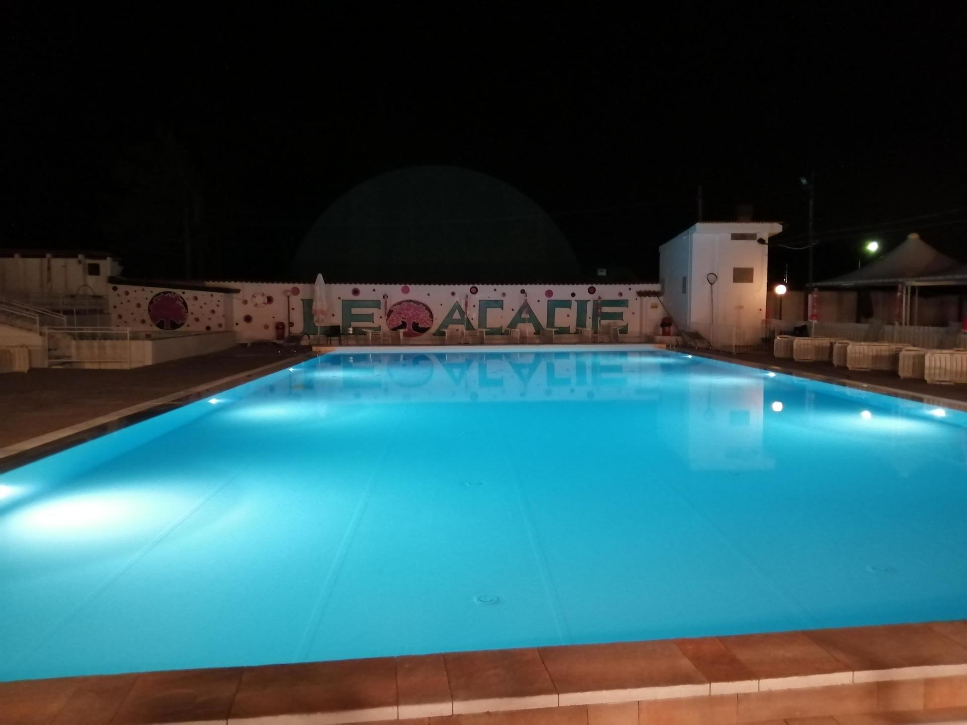 Piscina esterna illuminata di notte con acqua azzurra e terrazza decorata con murales.