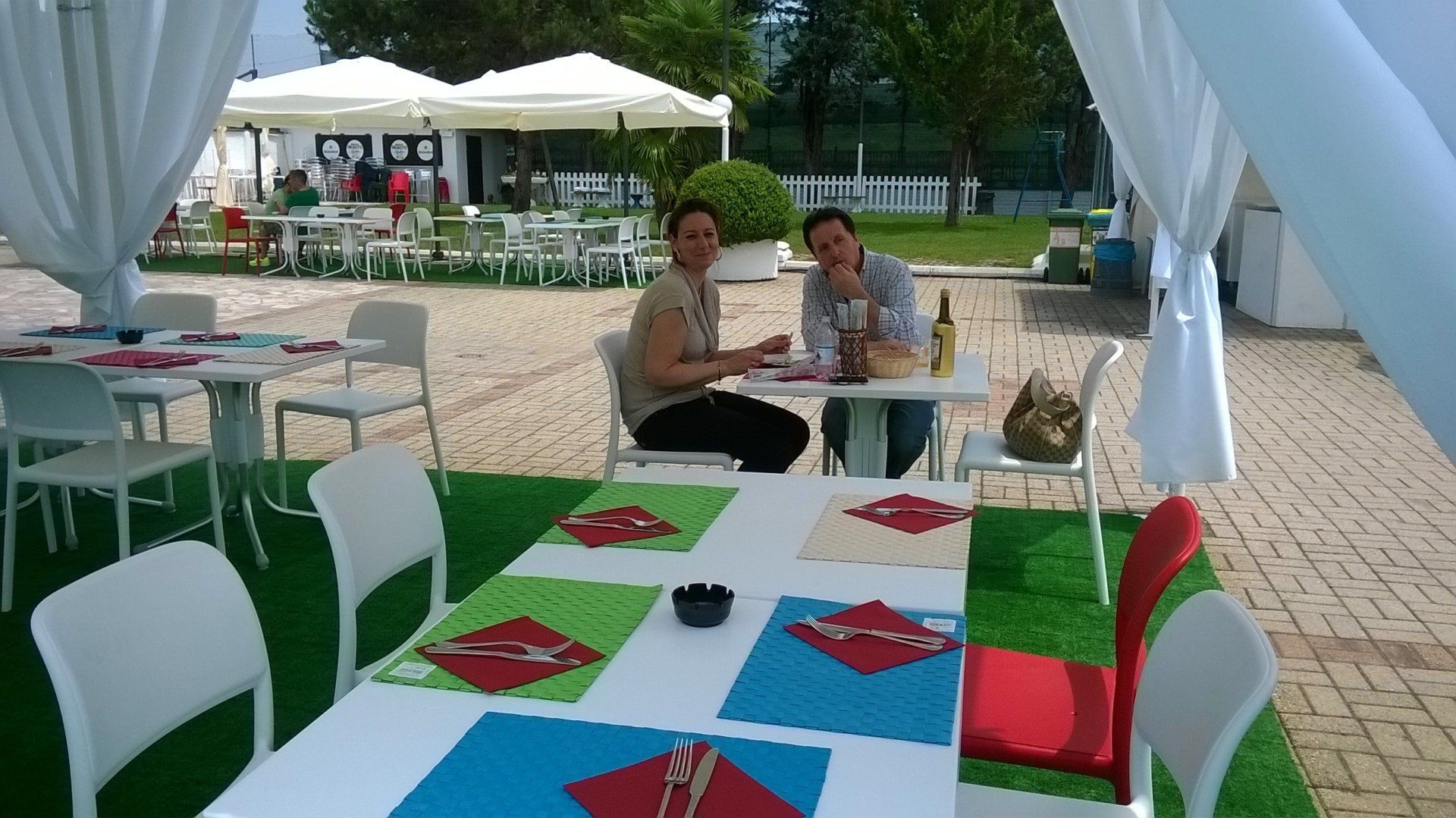 Tavolino da caffè all'aperto con due persone sedute sotto gli ombrelloni su un patio pavimentato.