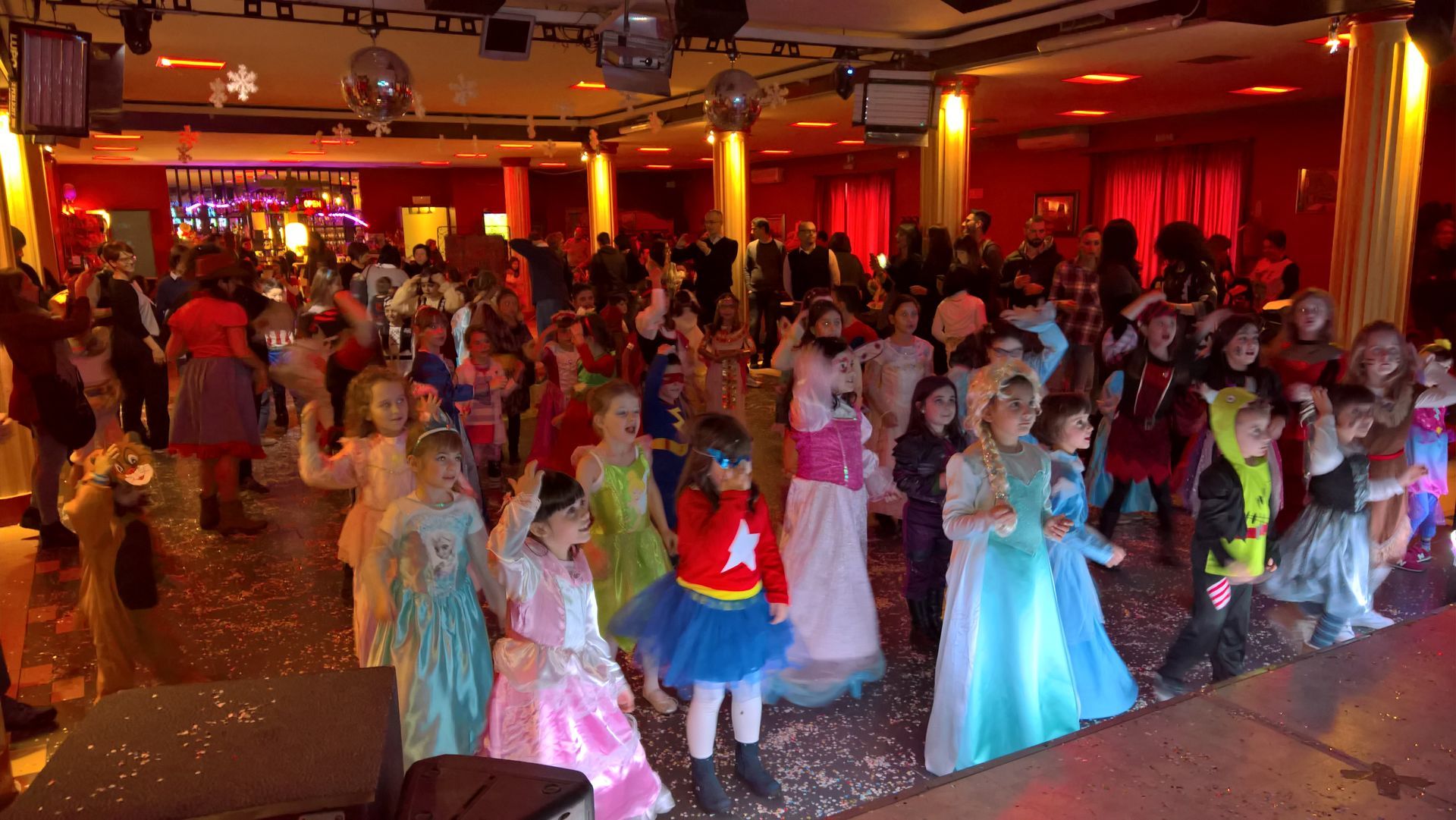 Una pista da ballo affollata di bambini in costumi colorati sotto una calda luce rossa