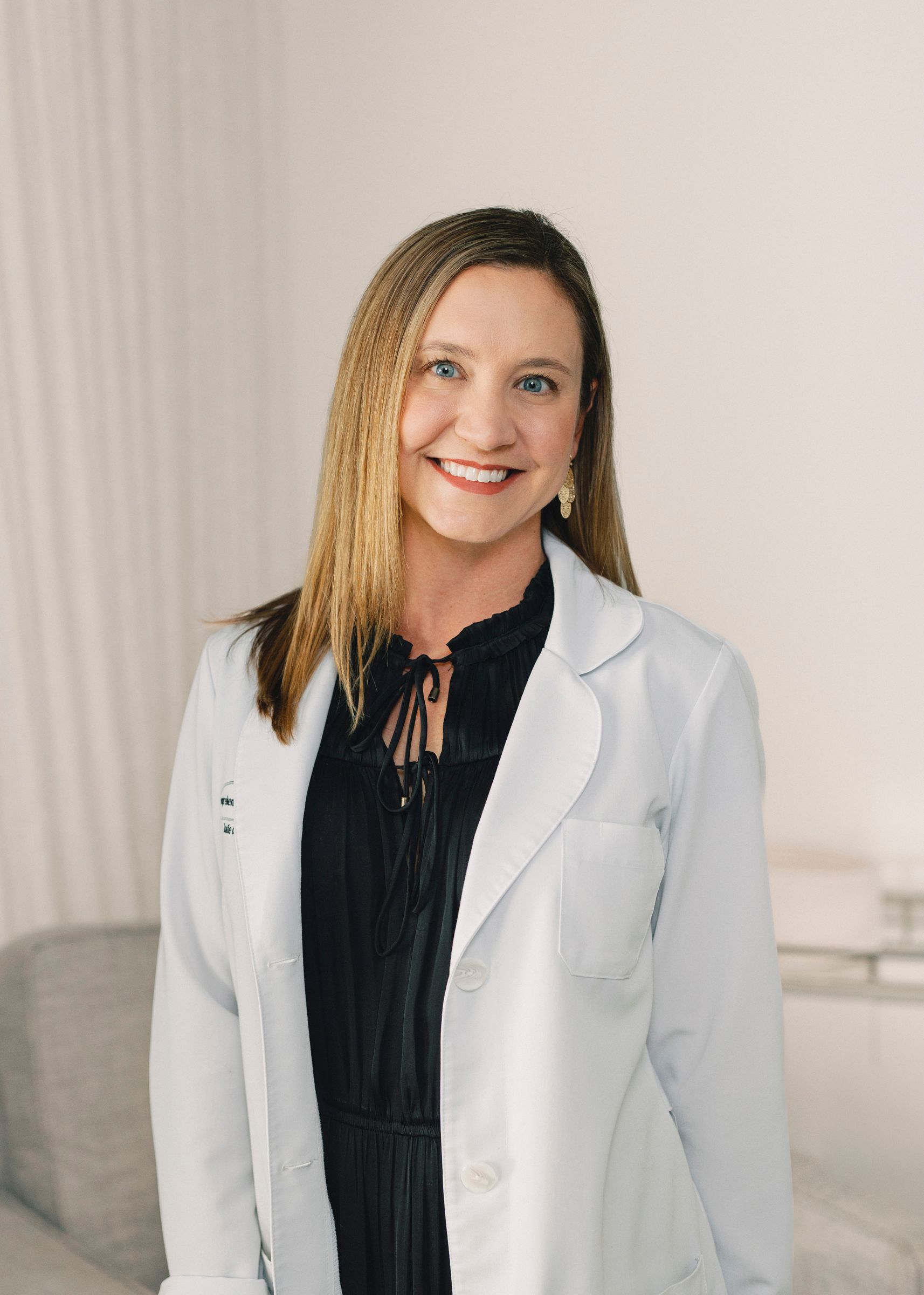 a portrait of Dr. Katie Osley, Board-Certified Dermatologist wearing a white blouse and gold long necklace