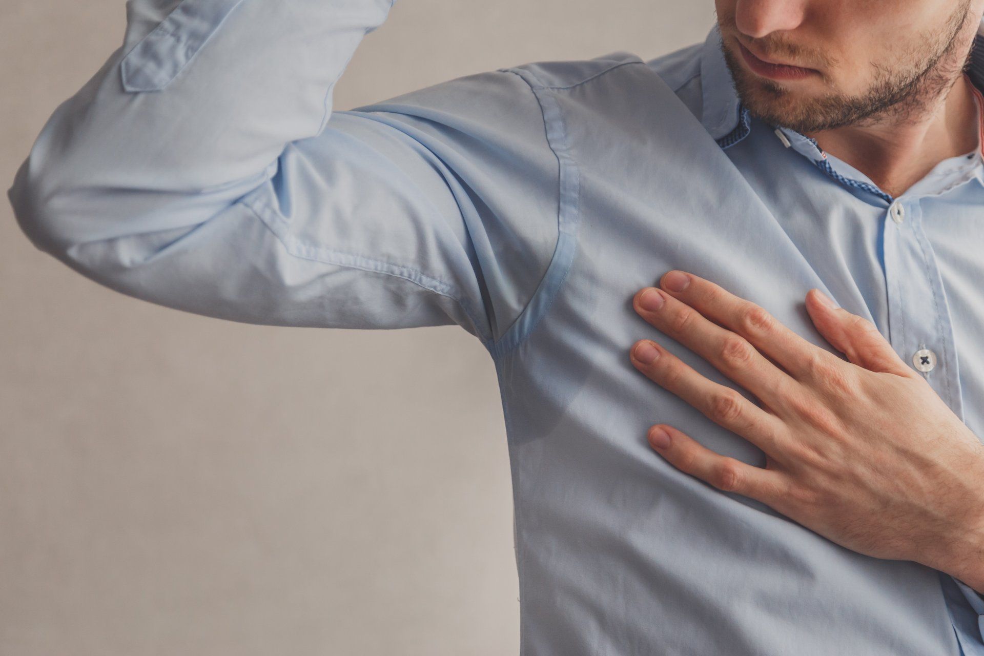 man lifting his right arm showing sweat stains on the armpits of his button down long sleeve shirt