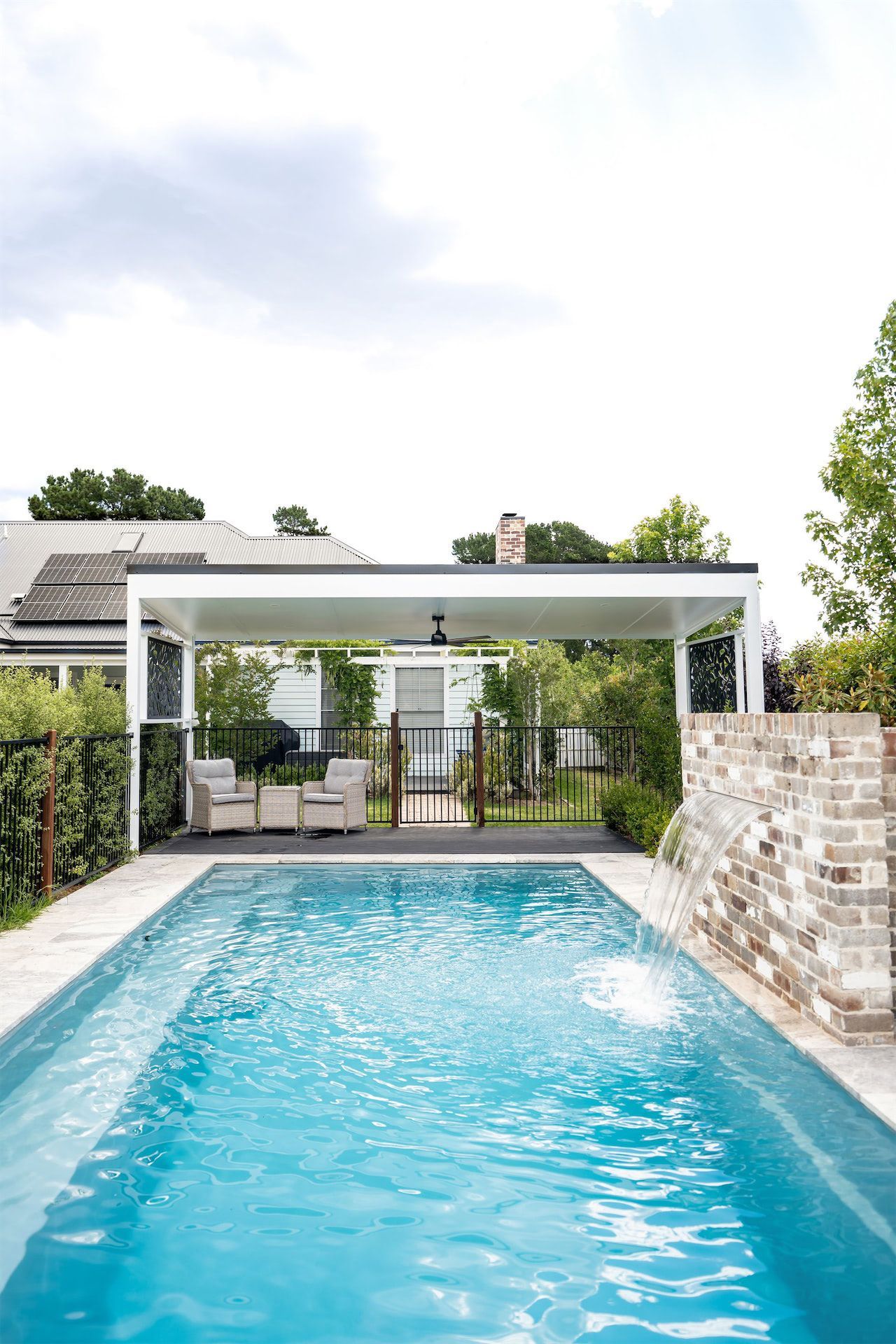 Backyard swimming pool with a white pergola, stone wall, and house in the background — Prime Built Group in Bowral, NSW