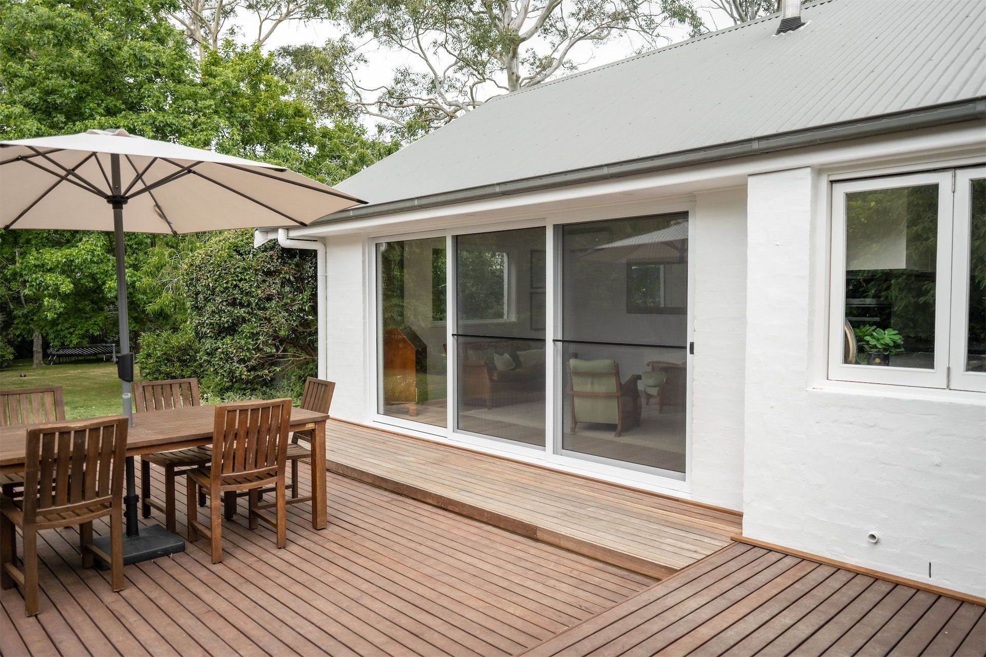 Patio deck with wooden table and umbrella beside a white house with large sliding glass doors — Prime Built in Bowral, NSW