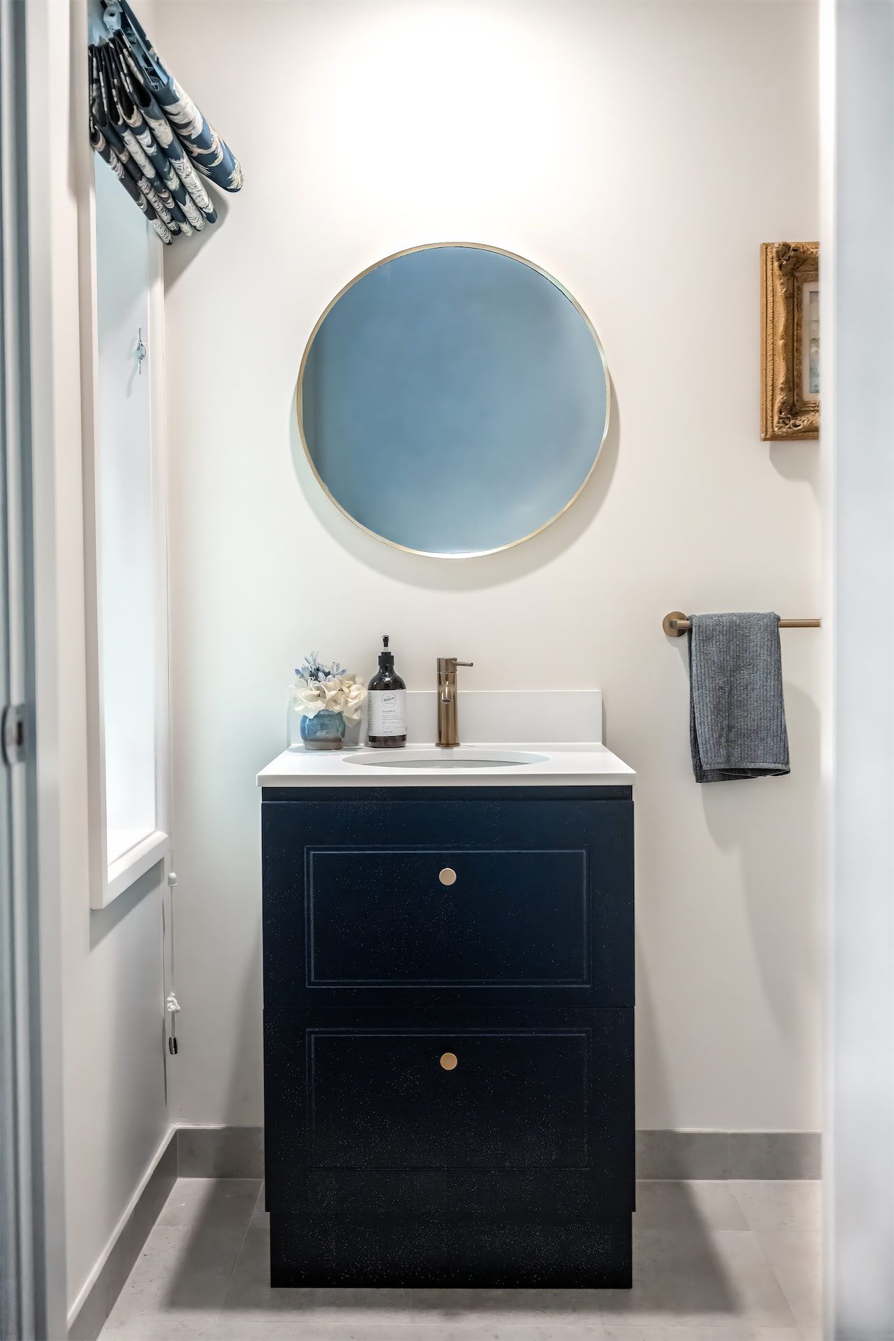 Small bathroom vanity with round mirror, navy cabinet, sink, and gray towel on white walls. — Prime Built in Bowral, NSW