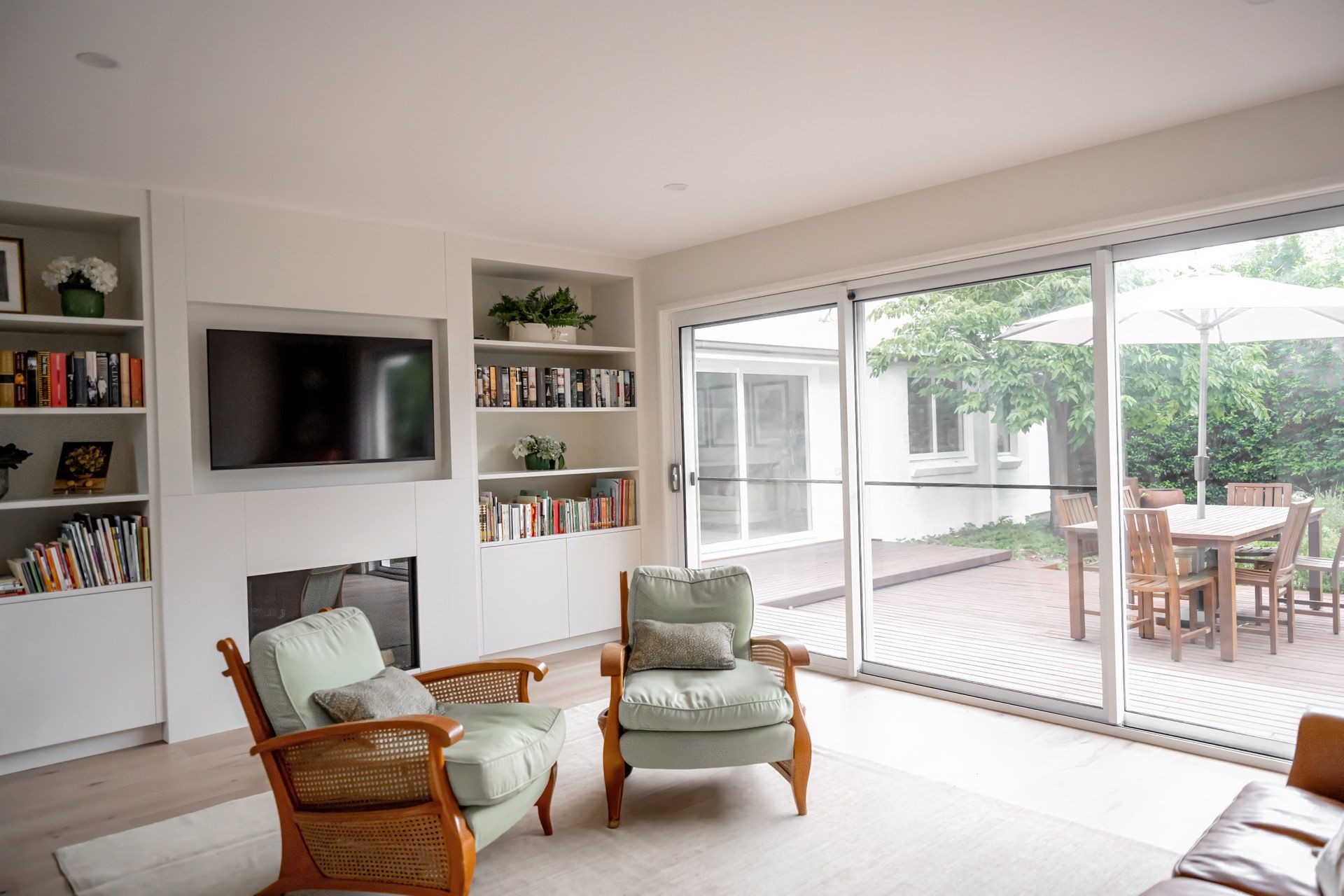 Bright living room with wall-mounted TV, armchairs, and sliding glass doors to a patio and garden. — Prime Built in Bowral, NSW