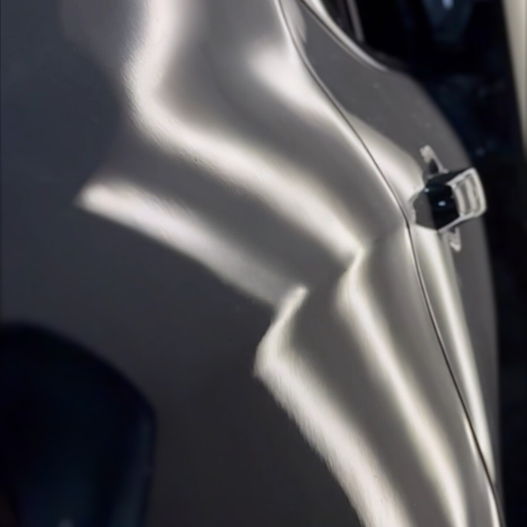 Silver car door with a large dent reflecting light.