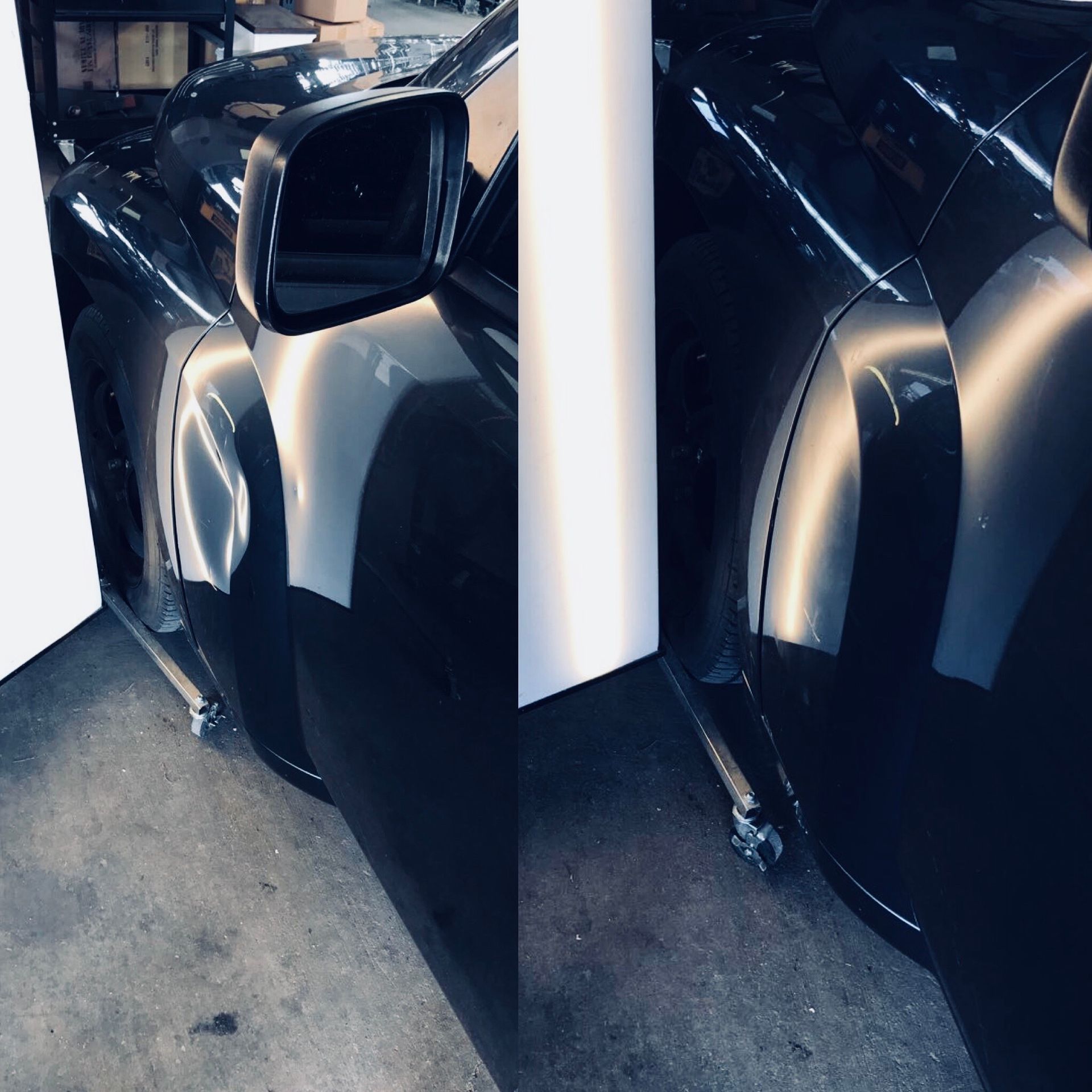 A black car with a dent in the front fender is parked inside a garage.