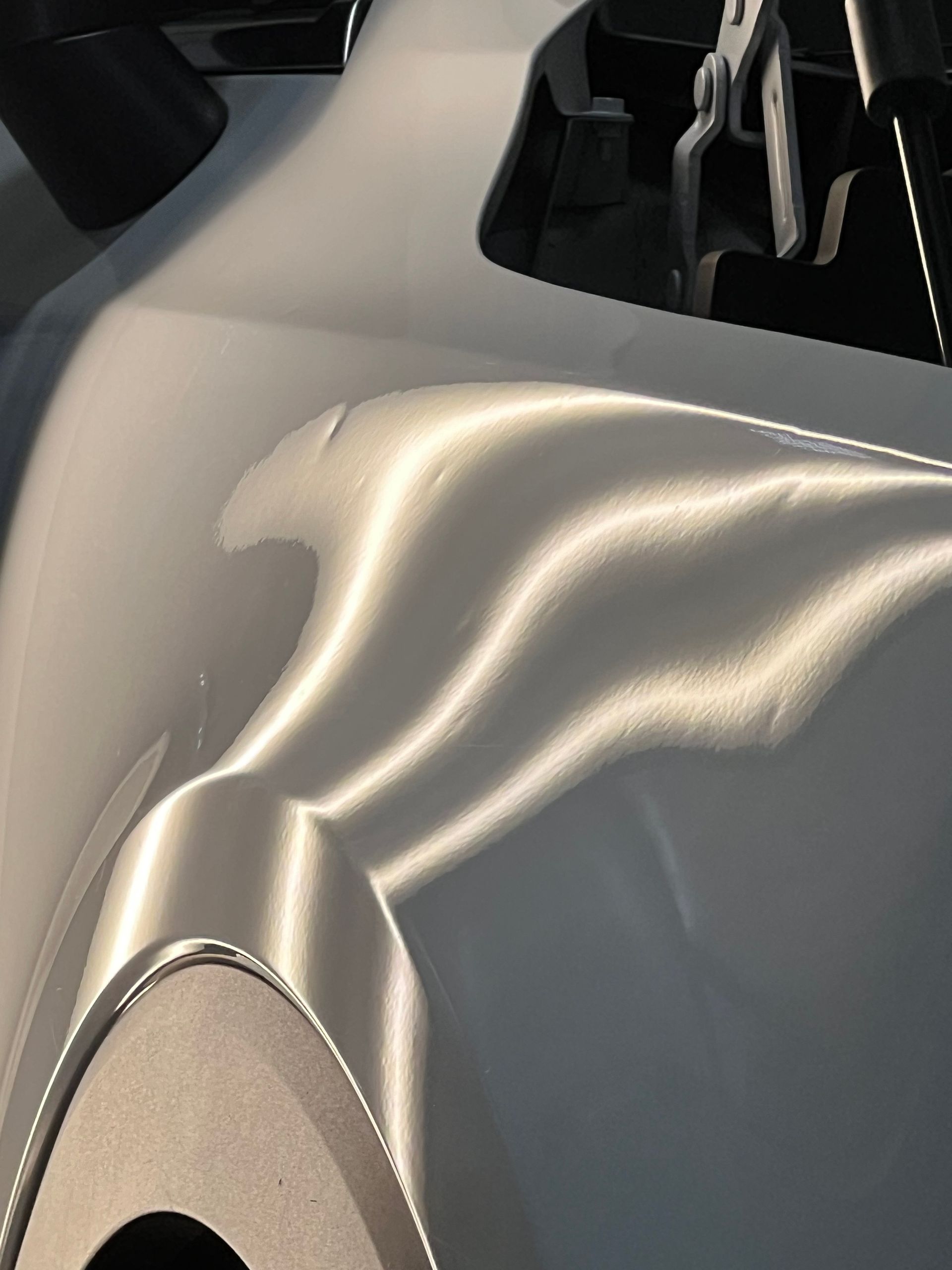 White car panel with multiple dents, reflecting bright light.