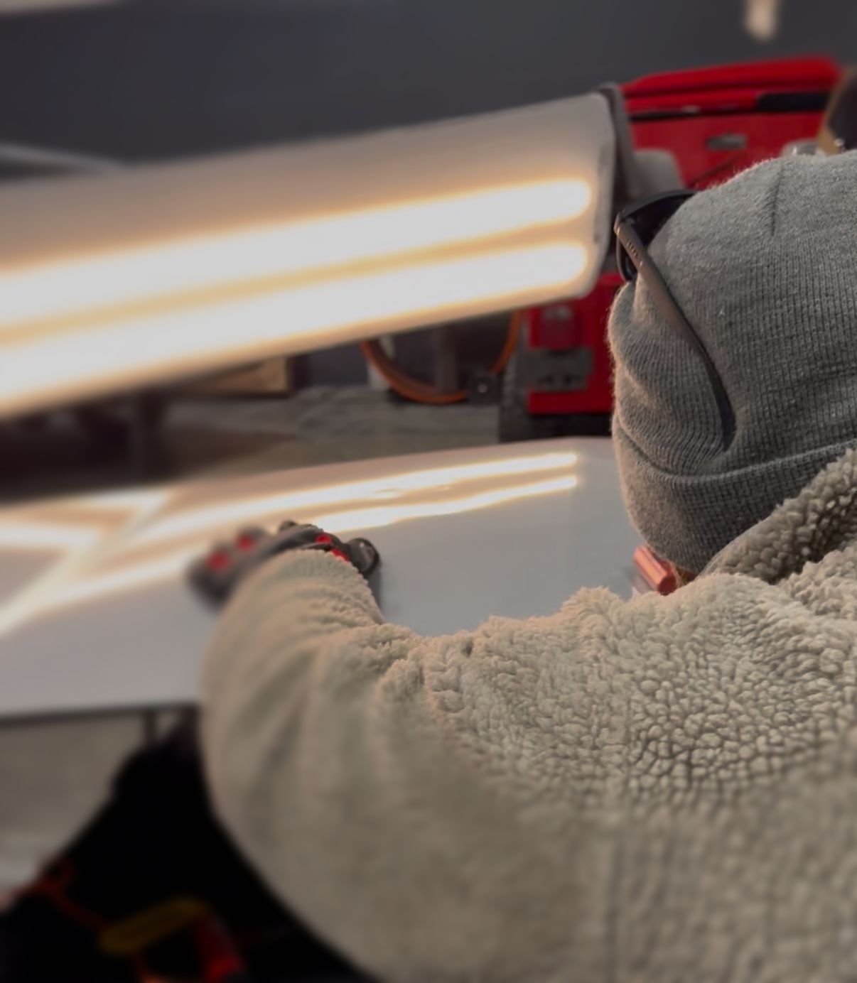 Person using a dent repair light to examine a car panel, likely for paintless dent removal.