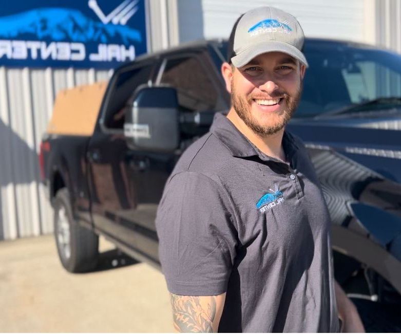 Man smiling in front of a black truck, wearing a hat and polo shirt with logo
