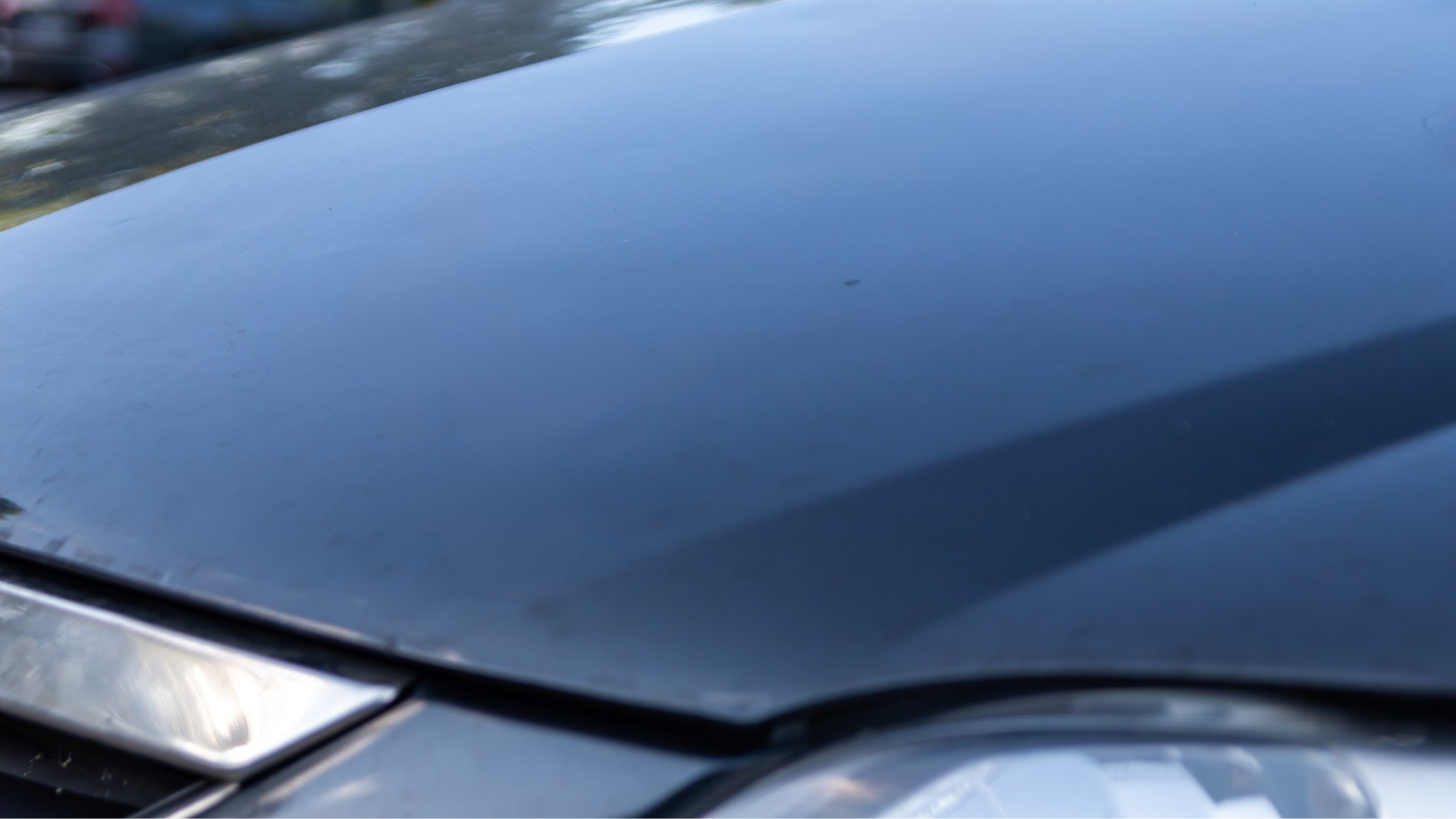 Black car hood reflecting sky and surroundings.
