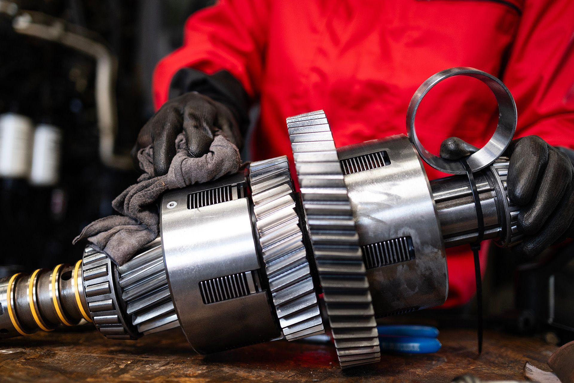 Gloved worker holding a metal mechanical part with gears on a workbench