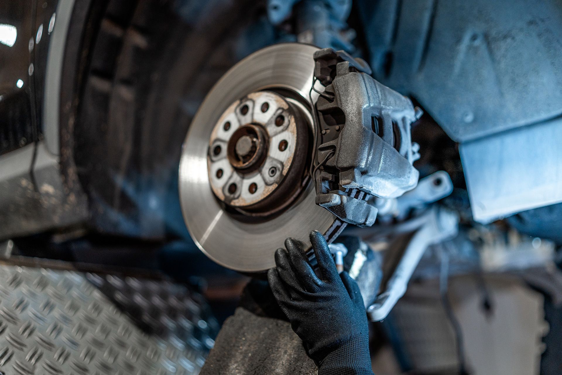 Mechanic using a gloved hand to service a car’s brake rotor and caliper in a garage