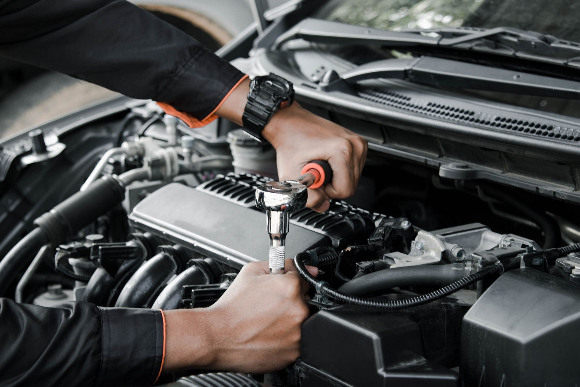 Mechanic using a ratchet wrench to repair an engine under a car hood