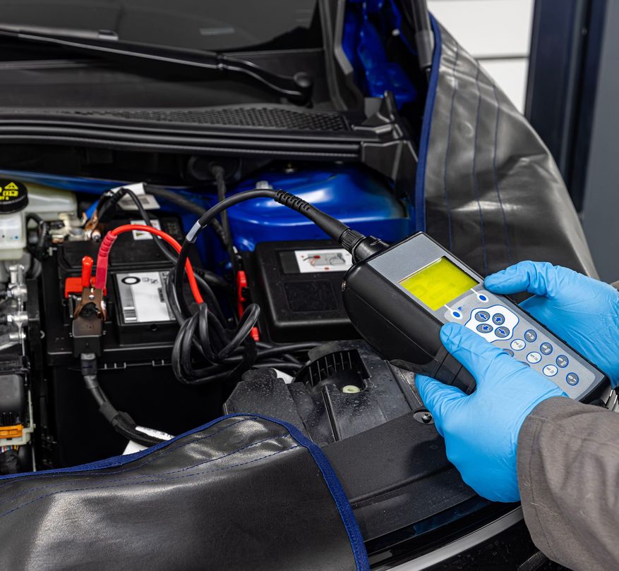 Blue-gloved hand uses a handheld scanner on a car engine in a garage