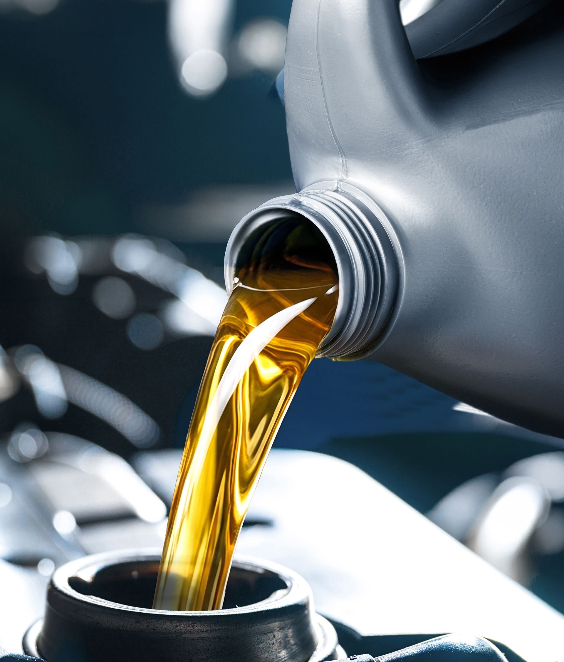 Golden motor oil pouring from a gray container into an engine fill cap