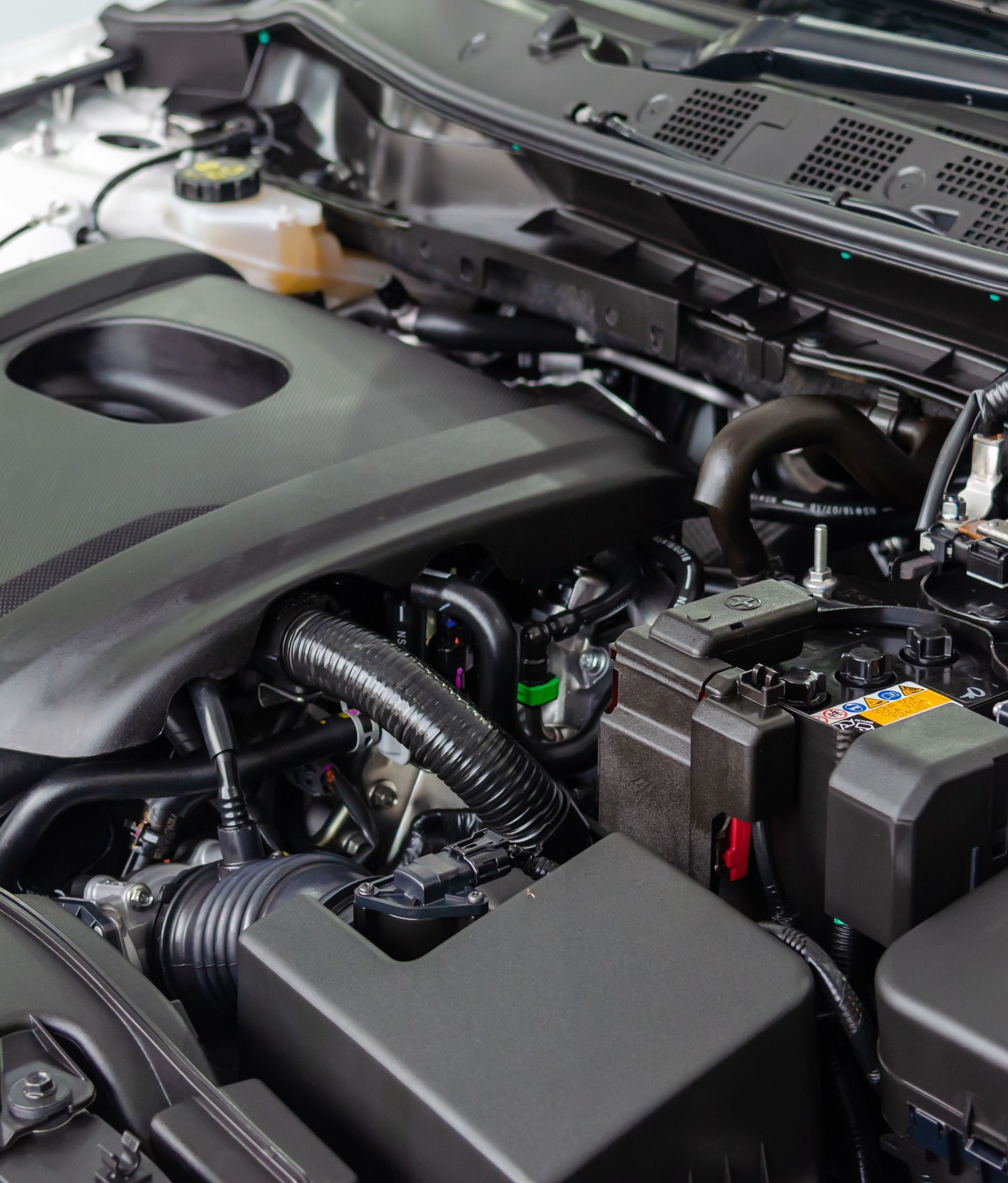 Car engine bay with black plastic covers, hoses, and battery components visible