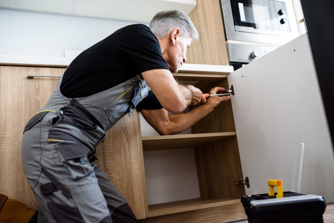 Worker installing a cabinet in a kitchen, leaning over with a drill and tools nearby