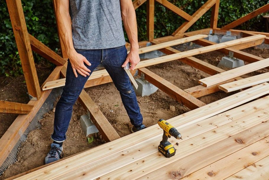 Person standing on wooden floor framing with a cordless drill nearby during construction
