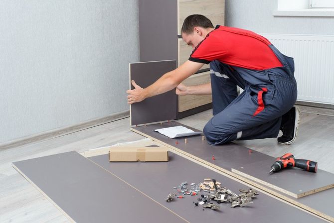 Man kneeling on a floor installing dark panels with tools and hardware nearby