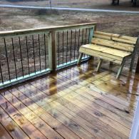 A wooden deck with a built-in bench and a railing with dark vertical metal balusters overlooks a dirt yard.