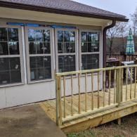 A wooden deck with railings attached to the side of a house featuring several large, grid-patterned windows.