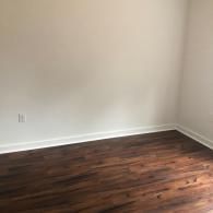 An empty room corner with white walls, white baseboards, and dark wood-look laminate flooring.