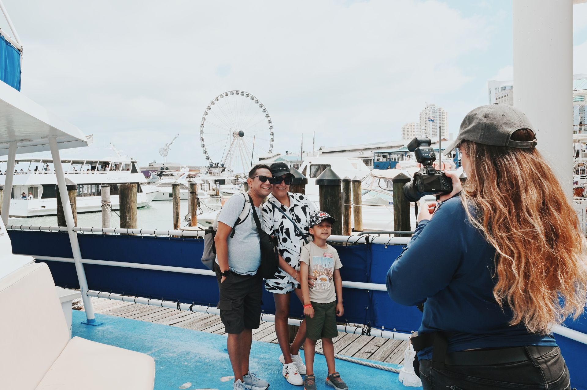 Family posing for a souvenir photo before boarding the Miami boat cruise at Bayside, with the Ferris wheel and downtown skyline in the background
