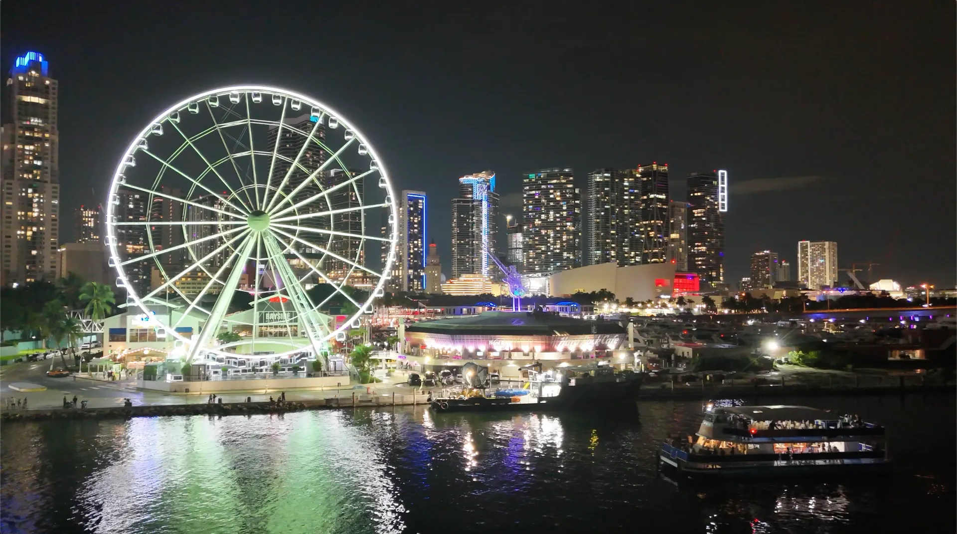 Best night cruise in Miami with Downtown skyline and Bayside Wheel illuminated at night.
