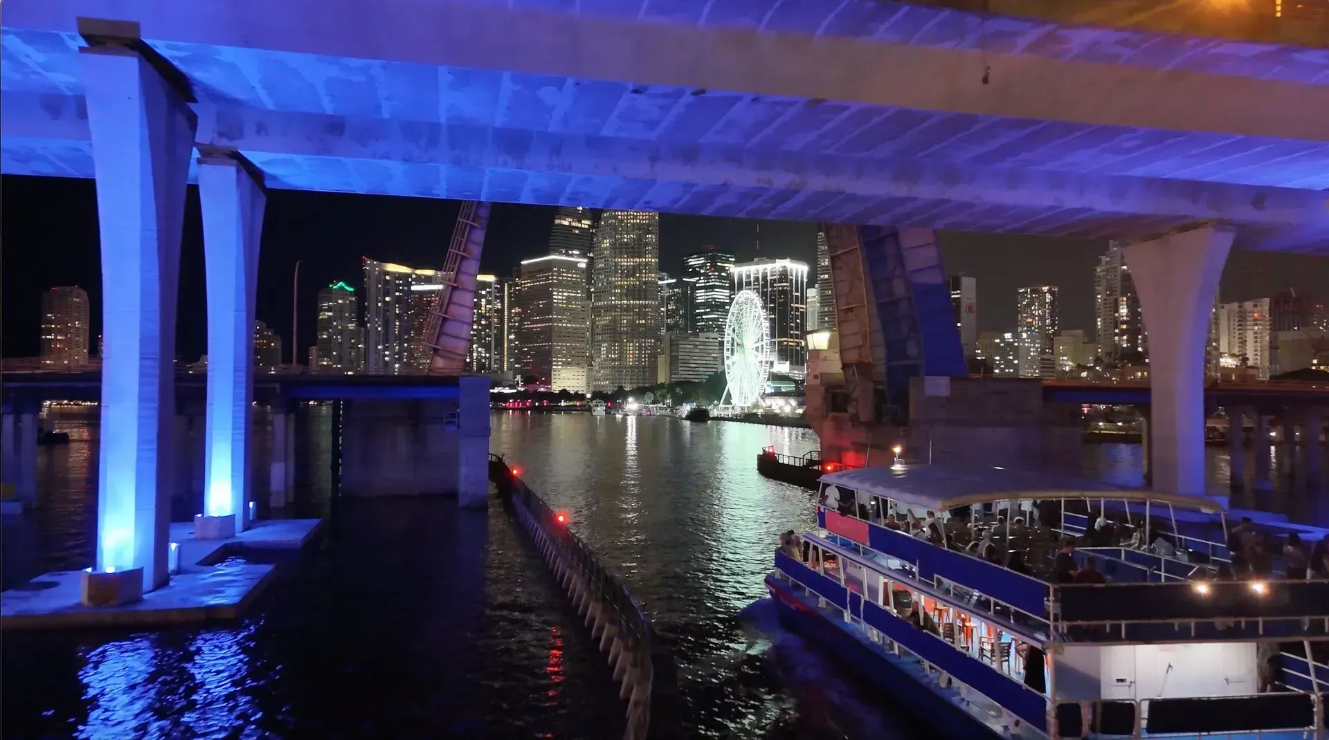 Nighttime sightseeing boat passing through Downtown Miami with skyline views and Biscayne Bay reflections