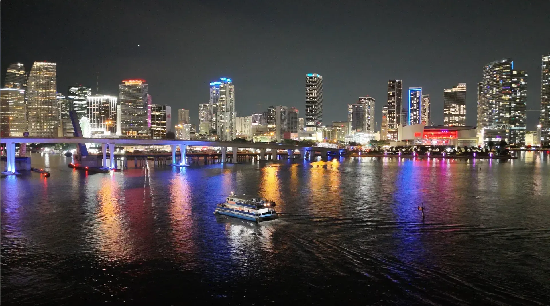 Panoramic nighttime views of Downtown Miami reflecting across Biscayne Bay with sightseeing boats on the water
