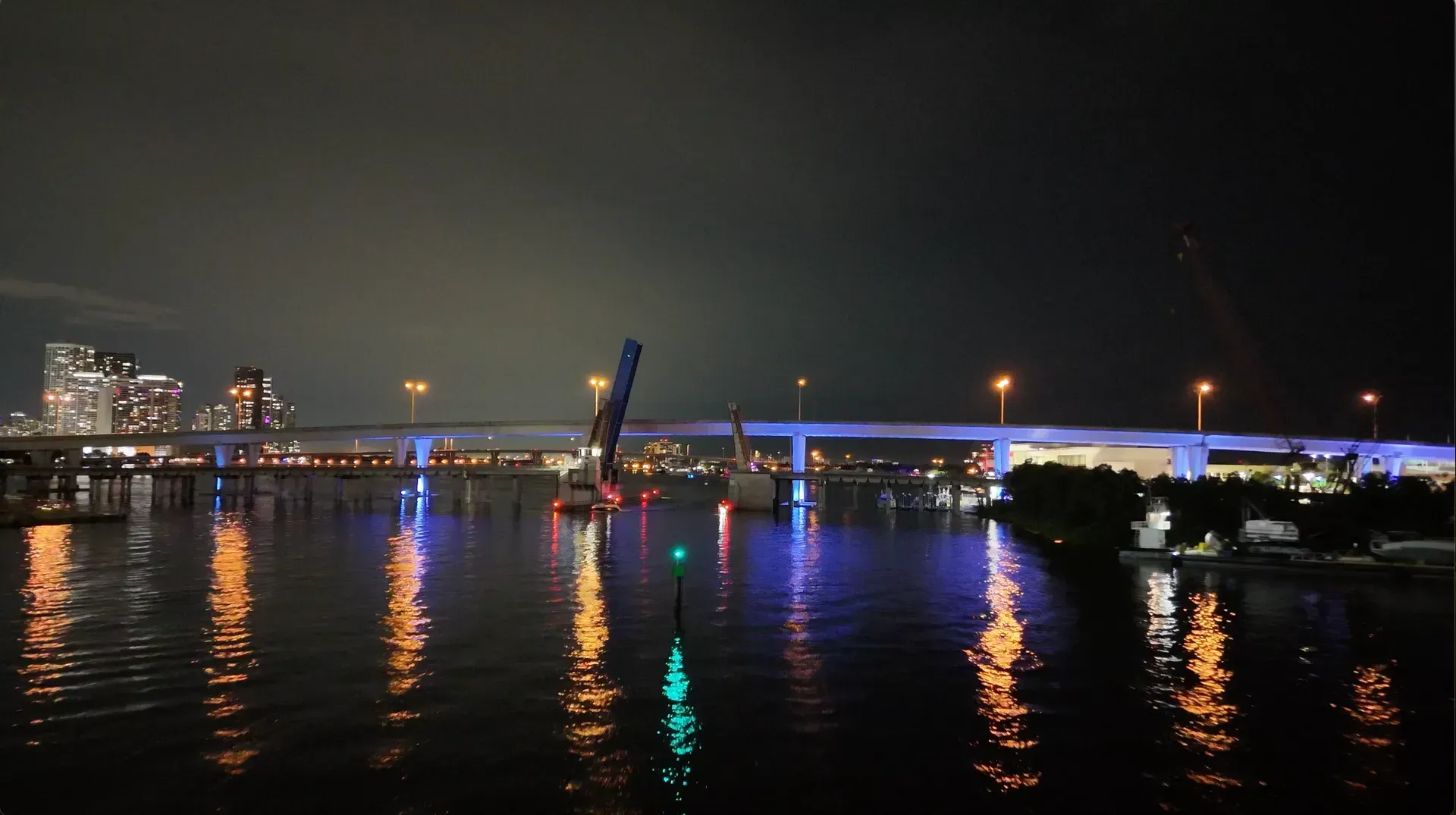 Illuminated waterfront bridge and colorful reflections across the water in Miami at night
